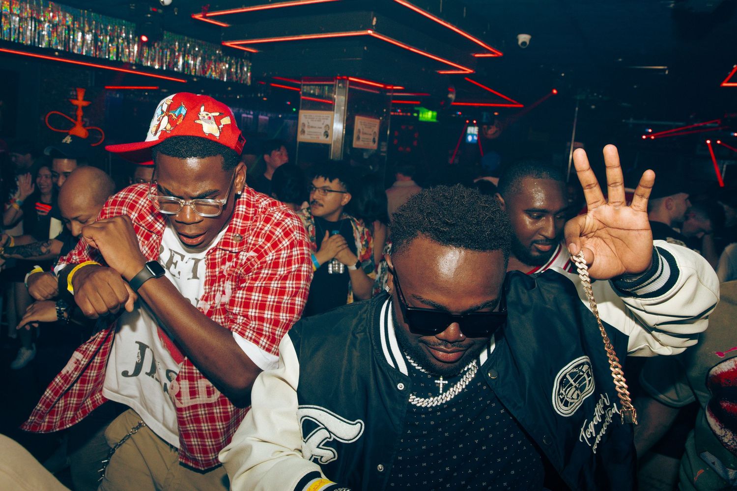 Three men dancing and celebrating at a nightclub party under colorful lights.