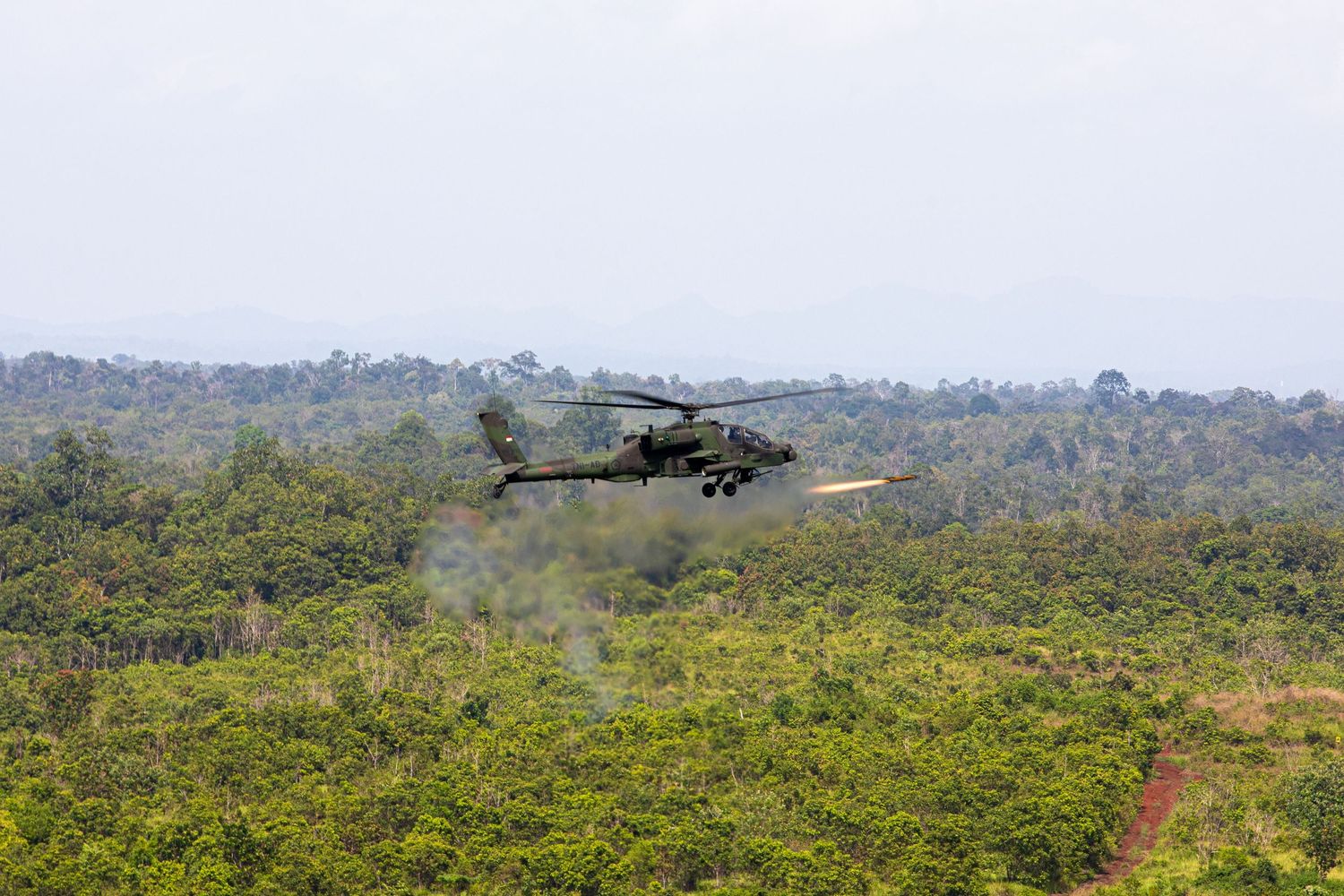 Military attack helicopter firing rockets over a dense tropical jungle landscape.