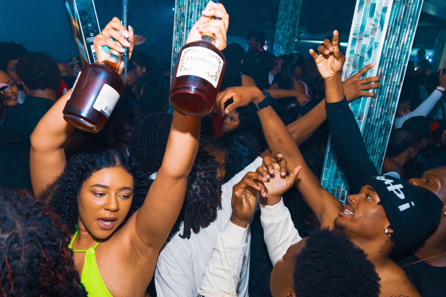 Energetic nightclub party scene with people dancing and holding liquor bottles under colorful lights.