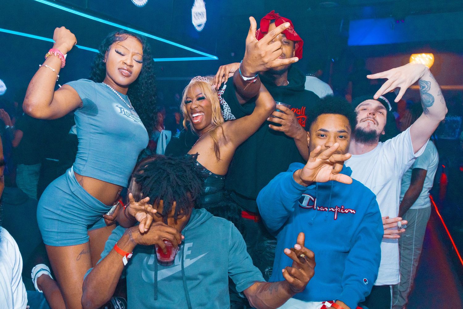 Group of friends dancing and celebrating together at a nightclub party, wearing casual blue outfits.