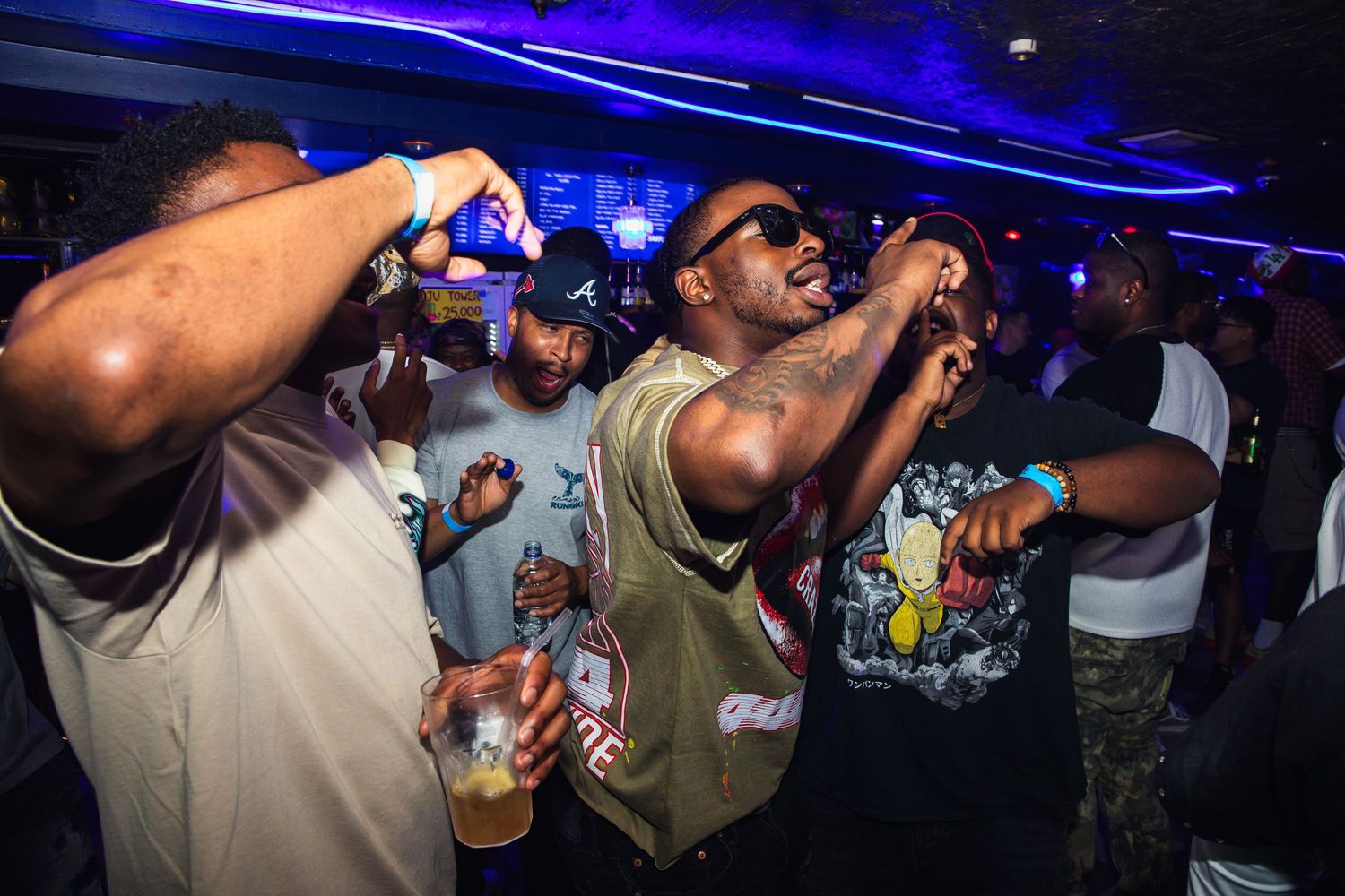 Men dancing and holding drinks at a lively nightclub event with blue lighting.