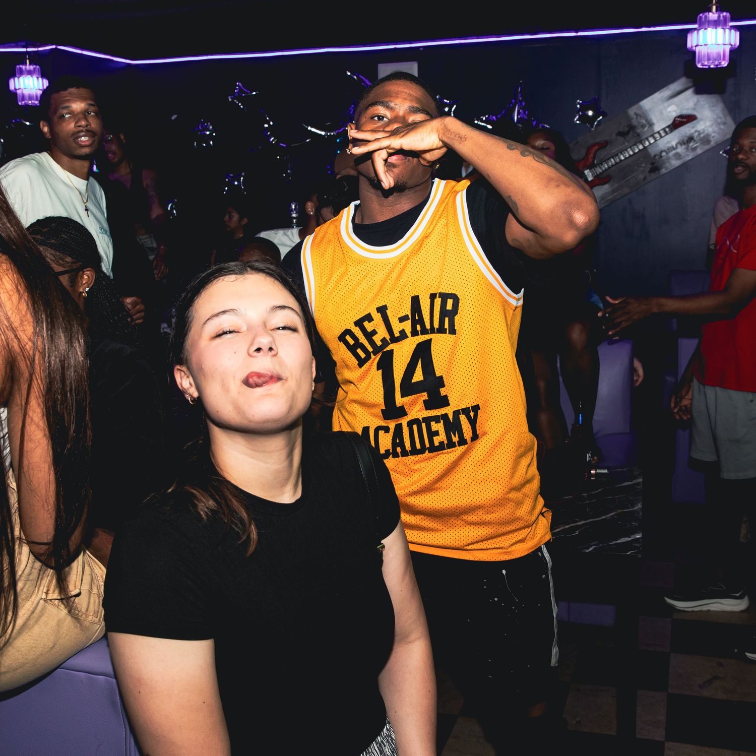 Young woman and man in Bel-Air Academy jersey enjoying a lively nightclub party.