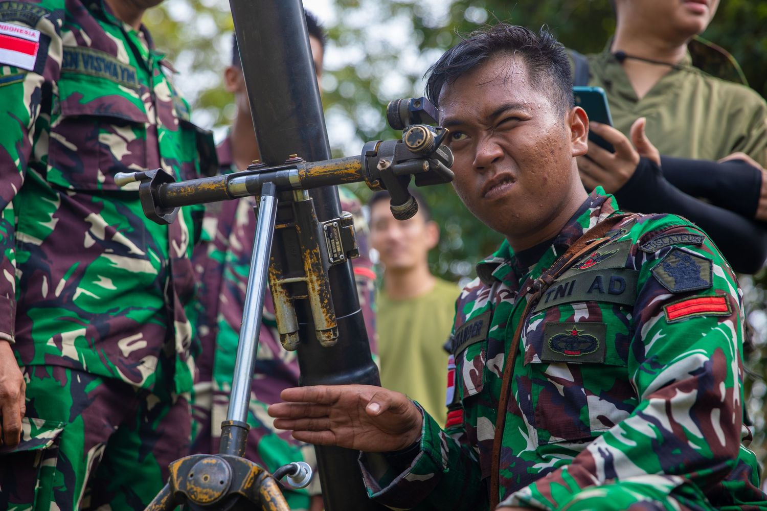Indonesian soldier in camouflage uniform handling a mortar weapon during military training exercise.