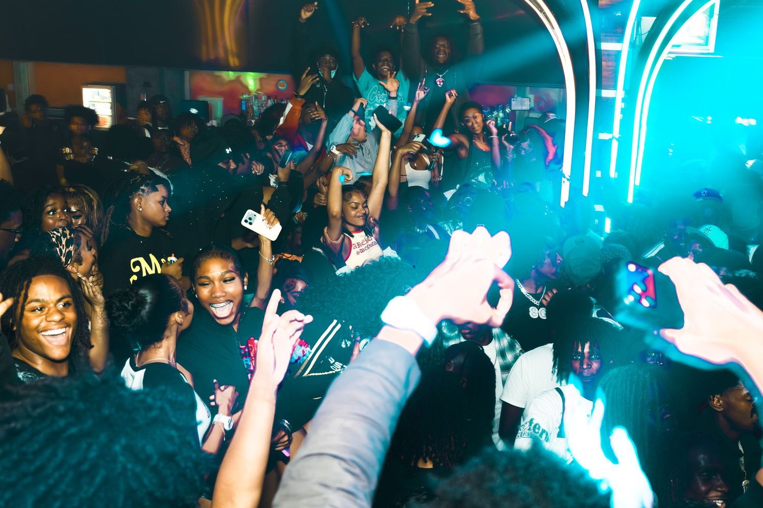 Energetic crowd dancing at a vibrant nightclub party with colorful blue neon lights and fog effects.