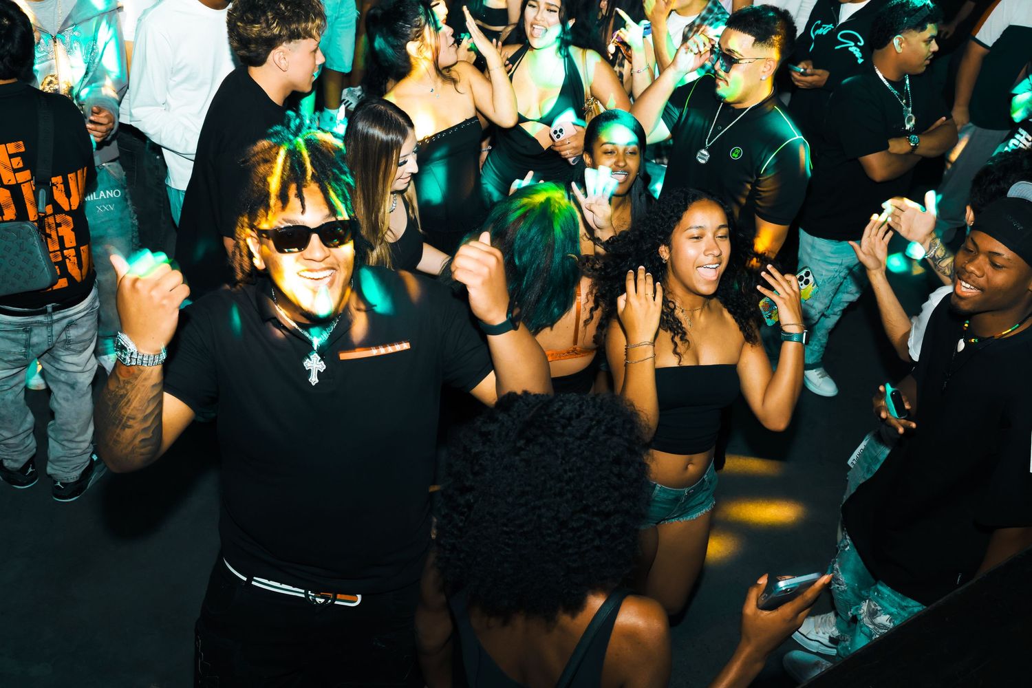 Young adults dancing and celebrating at a nightclub with teal lighting effects.