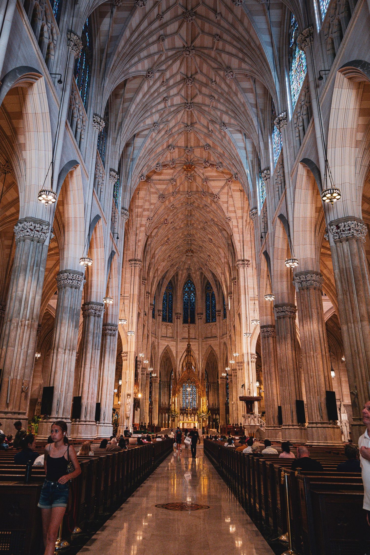 Interior of St. Patrick's Cathedral in NYC, featuring Gothic arches, ornate stone columns, and a long nave leading to the altar.