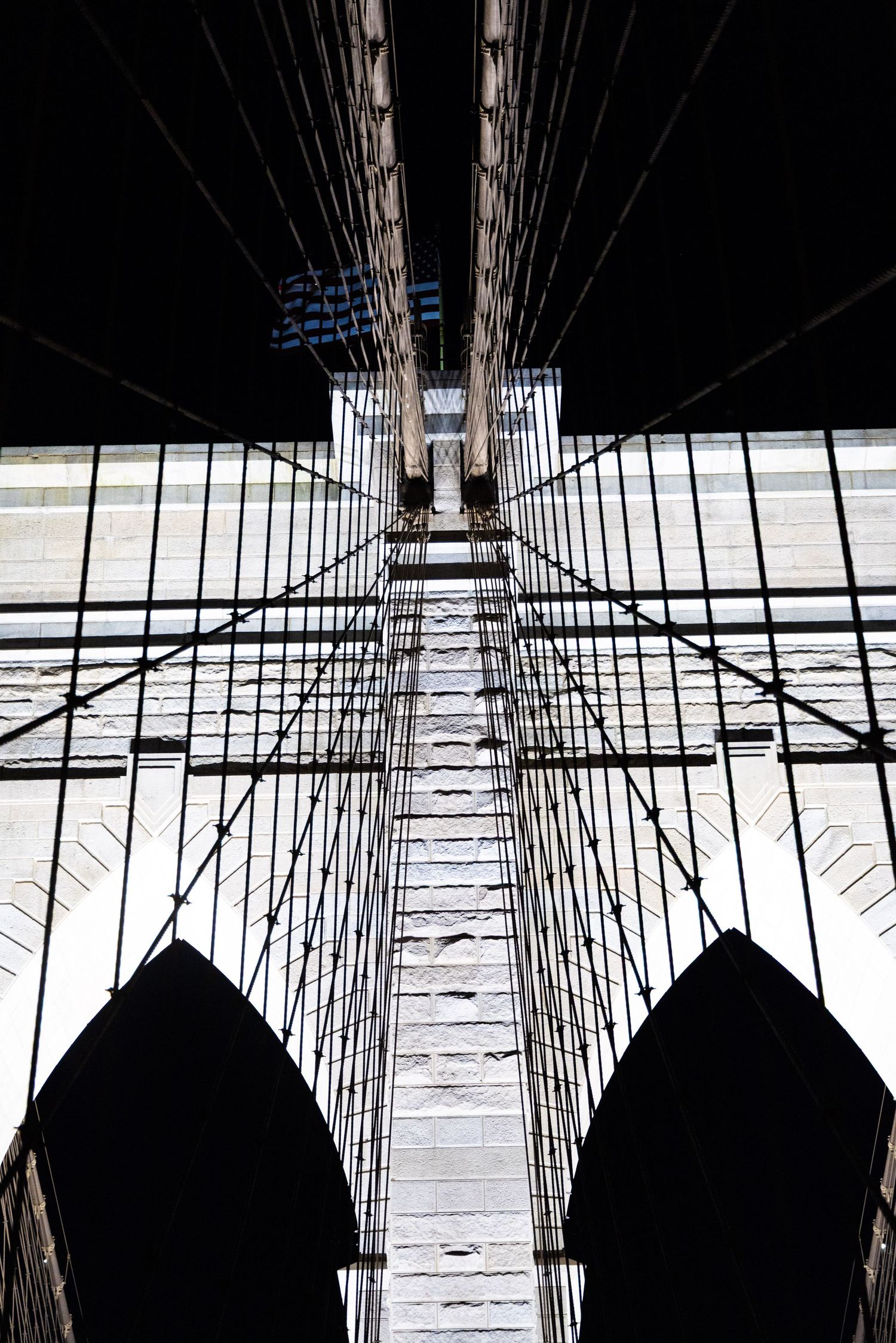 Looking straight up at the Brooklyn Bridge cables and towers creating a dramatic symmetrical perspective against the sky.