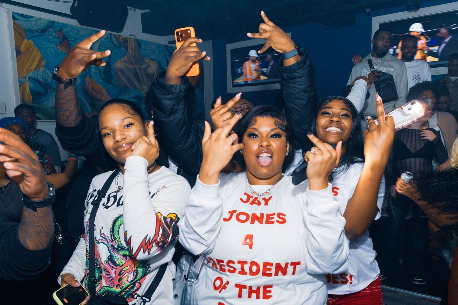 Group of young women celebrating at a party, one wearing a Jay Jones for President sweatshirt, dancing and having fun.