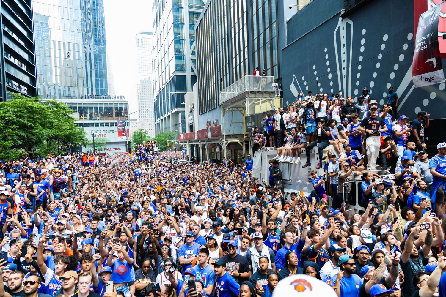 Massive crowd of fans in blue jerseys celebrating a championship parade on a city street surrounded by skyscrapers.