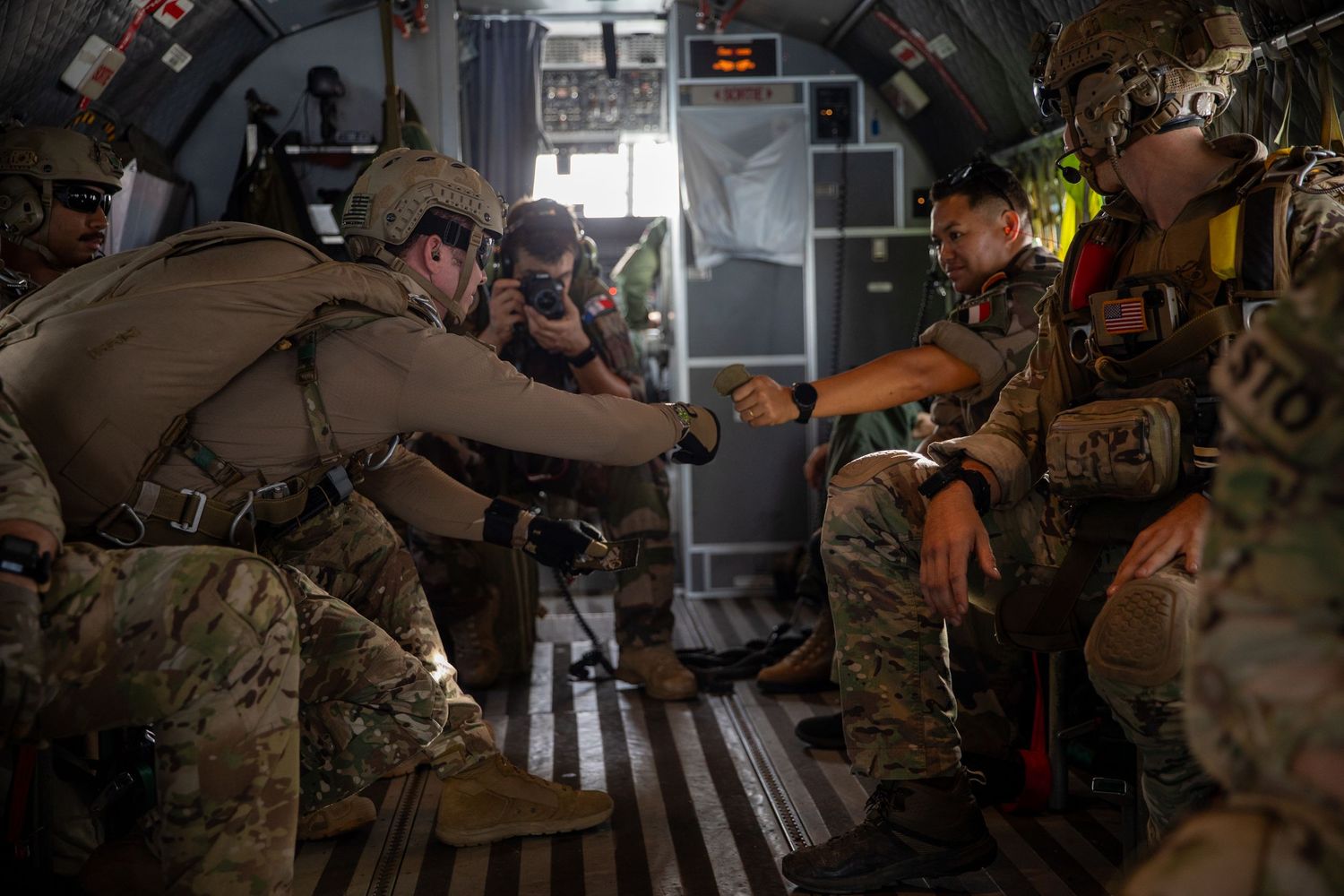 Military personnel inside an aircraft conduct pre-jump equipment checks before an airborne parachute operation.