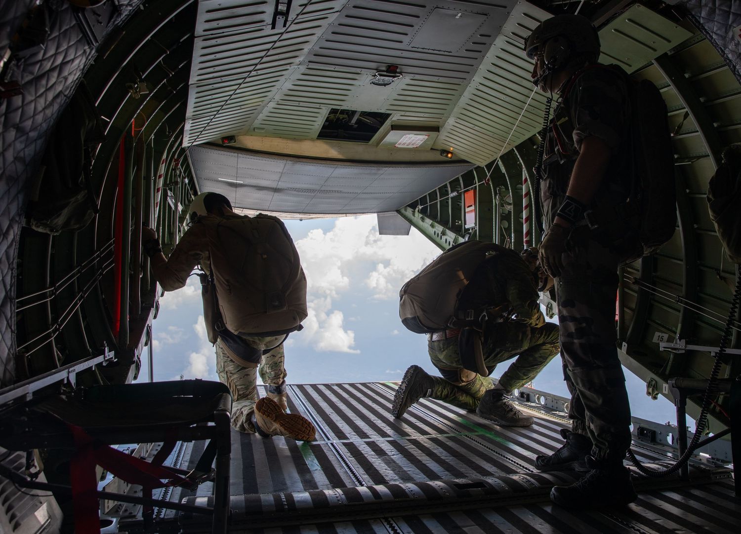 Two soldiers stand at the open ramp of a military aircraft preparing to conduct an airborne jump operation.
