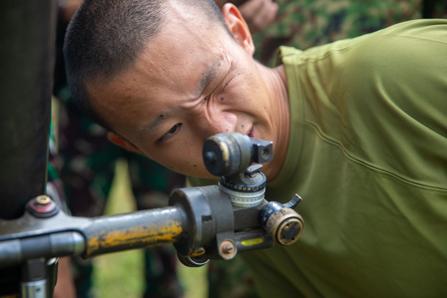 Military soldier in green uniform carefully aiming through a weapon sight during training.