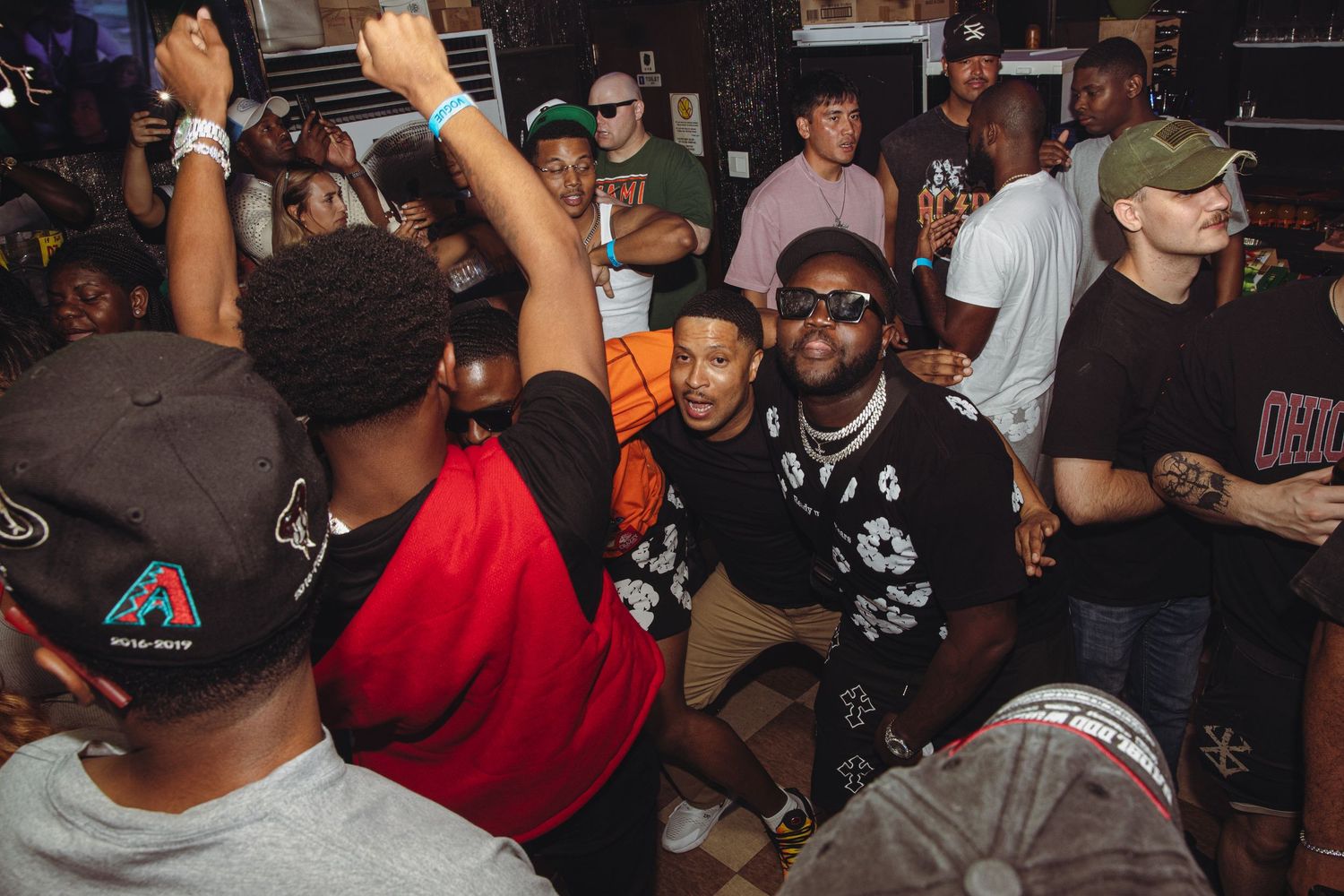 Large group of people enjoying a packed nightclub party with hands raised.
