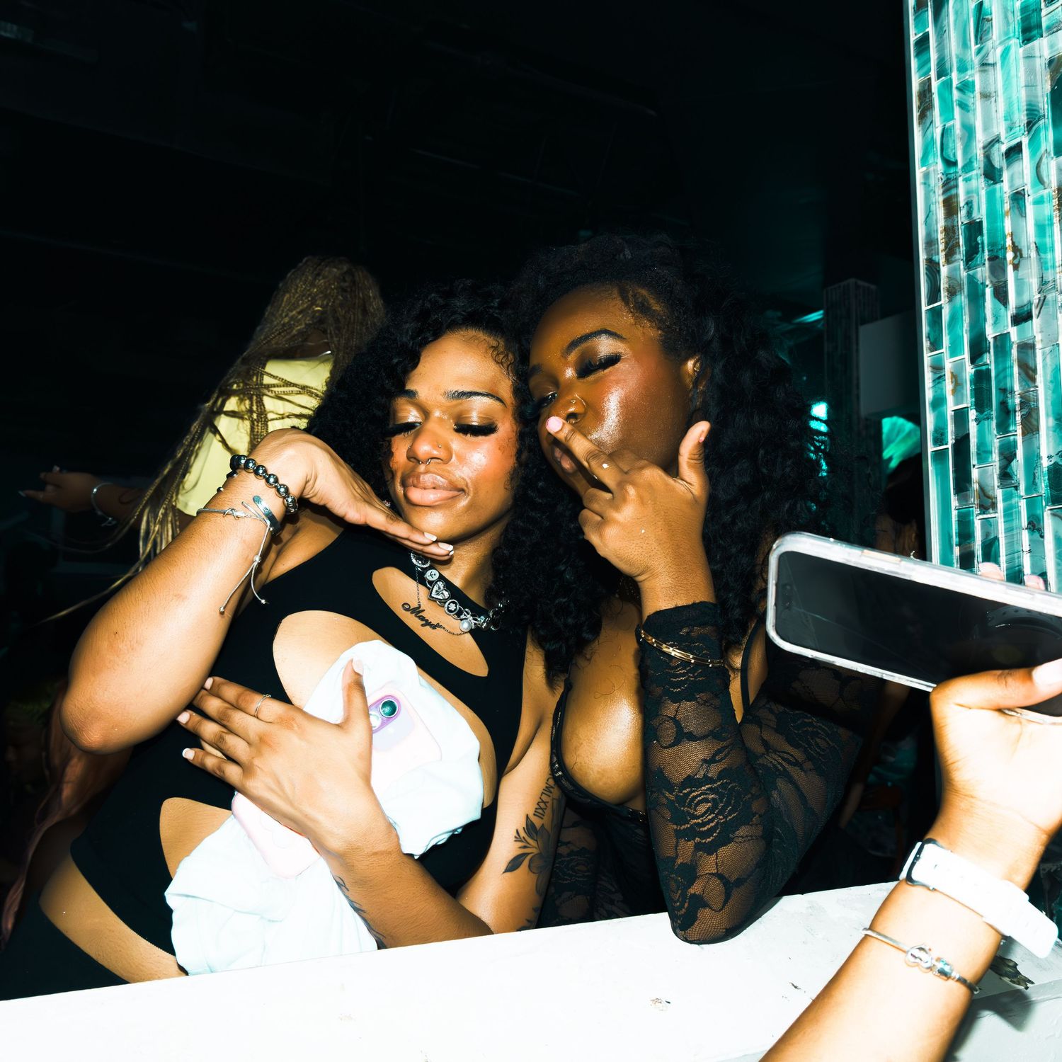 Two women posing together at a nightclub, smiling and making hand gestures in a dimly lit venue.