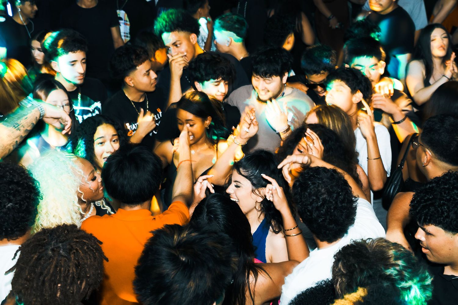 A diverse crowd of young people dancing and socializing at a lively indoor party with colorful lighting.