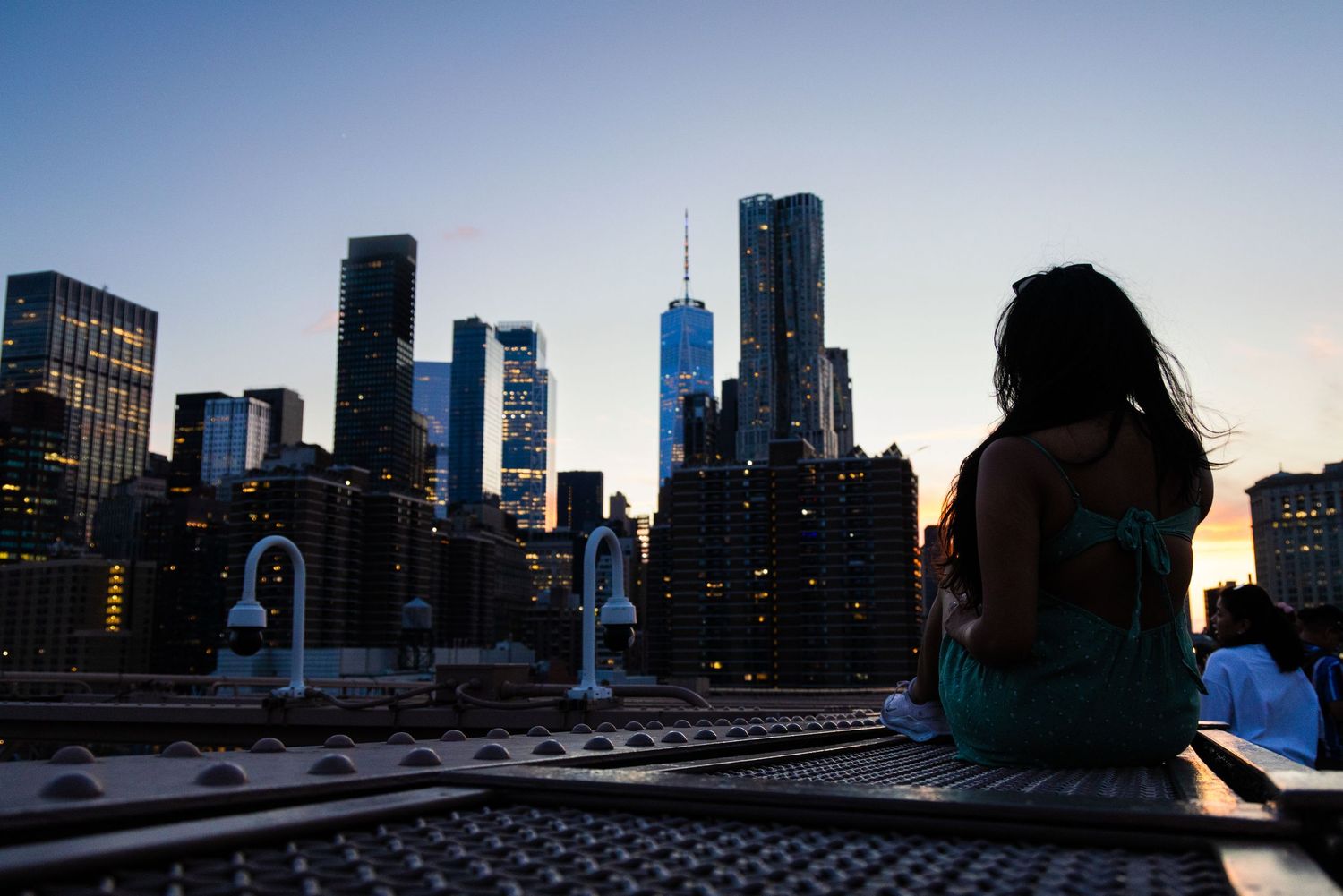 Woman sitting on a rooftop gazing at a stunning city skyline at dusk with illuminated skyscrapers.