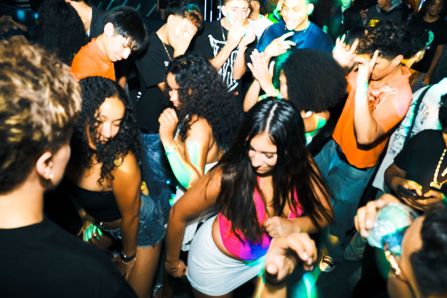 Diverse group of young people dancing energetically at a nightclub party under dim lighting.