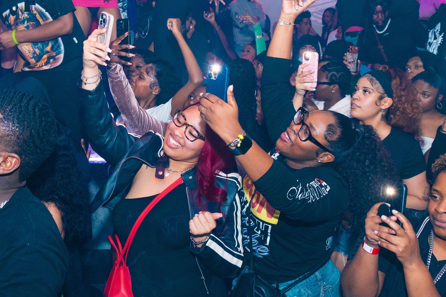 Excited crowd taking selfies with phones at a vibrant nightclub party event.