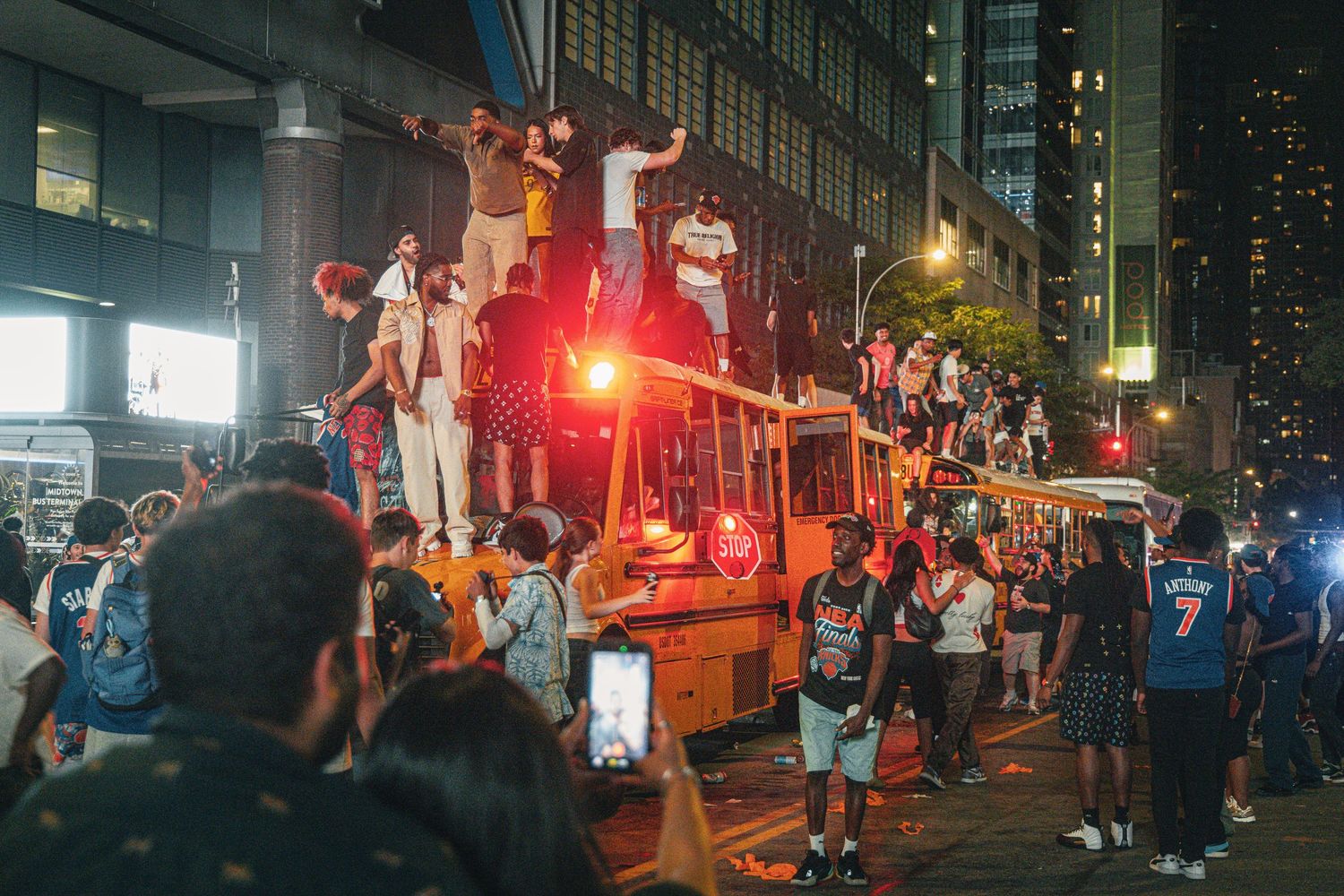 Crowd of people celebrating at night, climbing on construction equipment on a busy urban street.