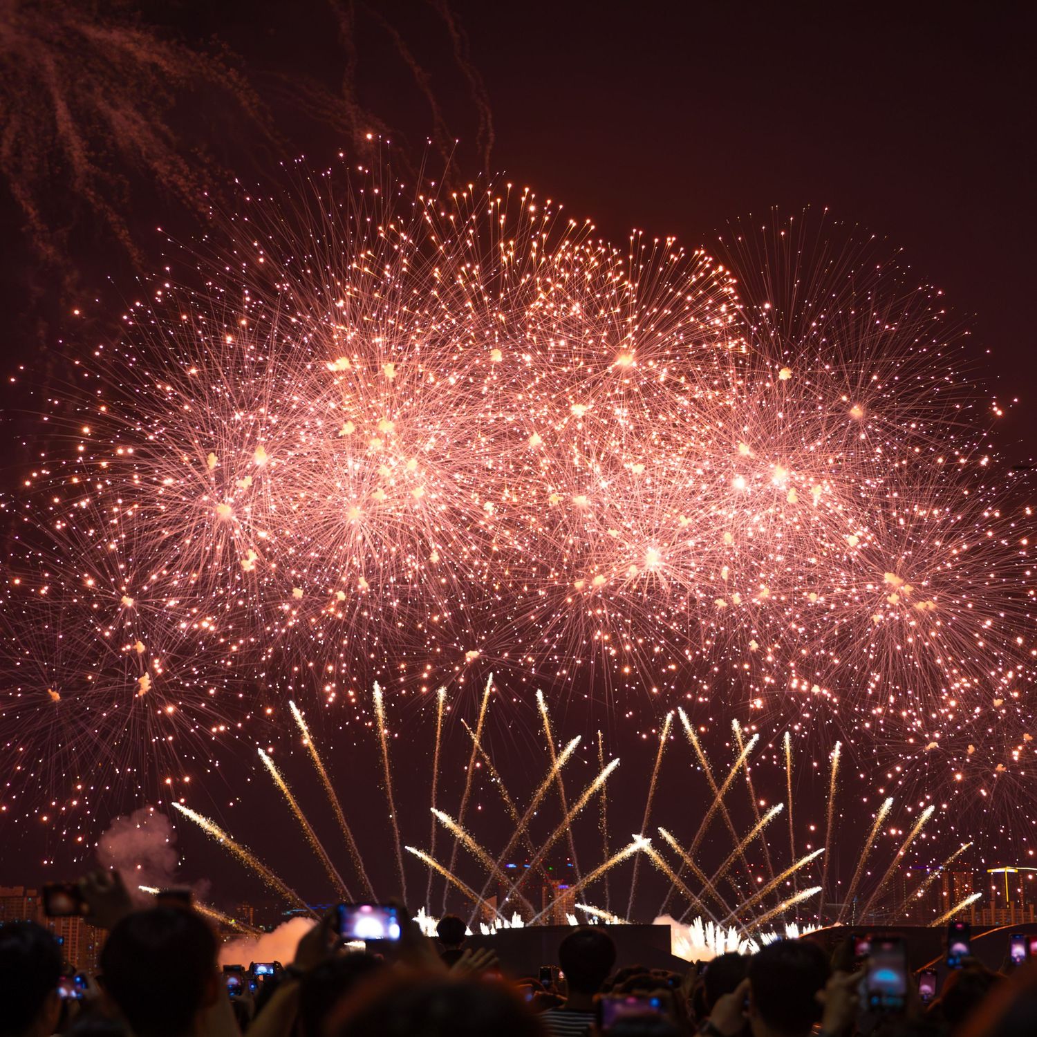 Dazzling golden fireworks bursting in the night sky as spectators watch and photograph the display.