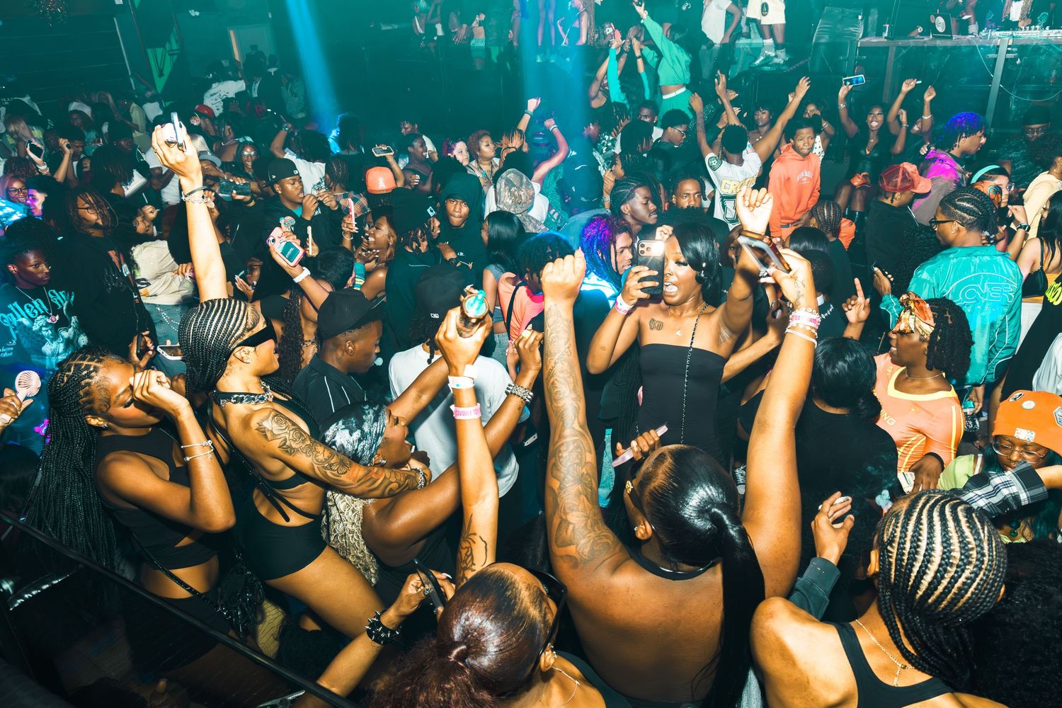 Energetic nightclub crowd dancing and celebrating under colorful lights at a packed party event.
