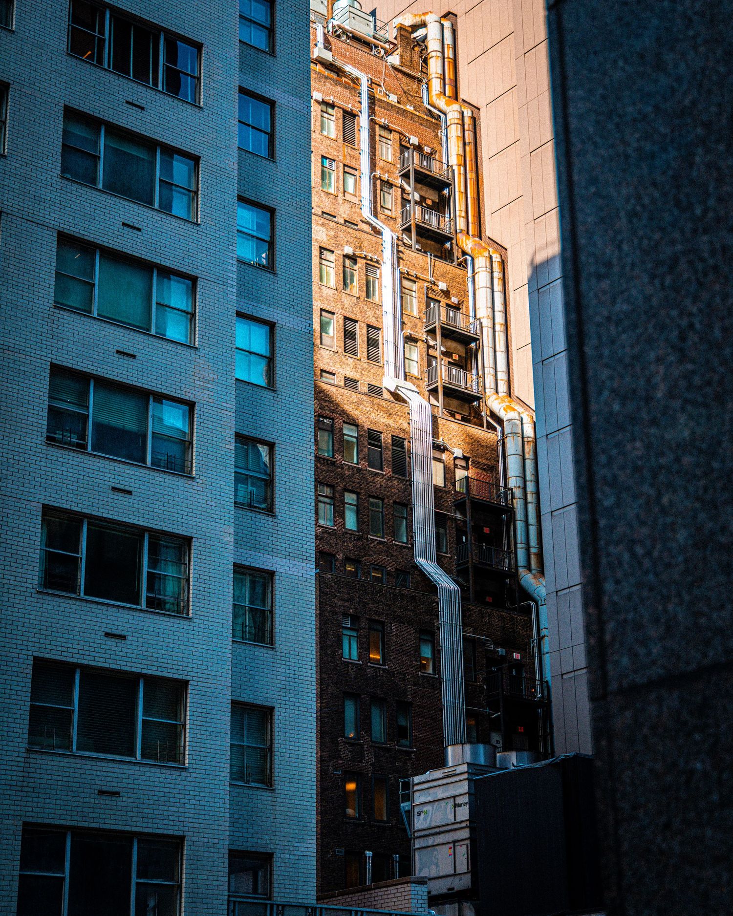 Urban canyon view of contrasting modern white and vintage brick skyscrapers bathed in golden sunlight between narrow city gaps.