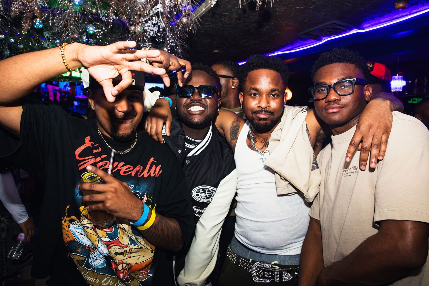 Four men smiling and posing together at a nightclub party with festive decor.