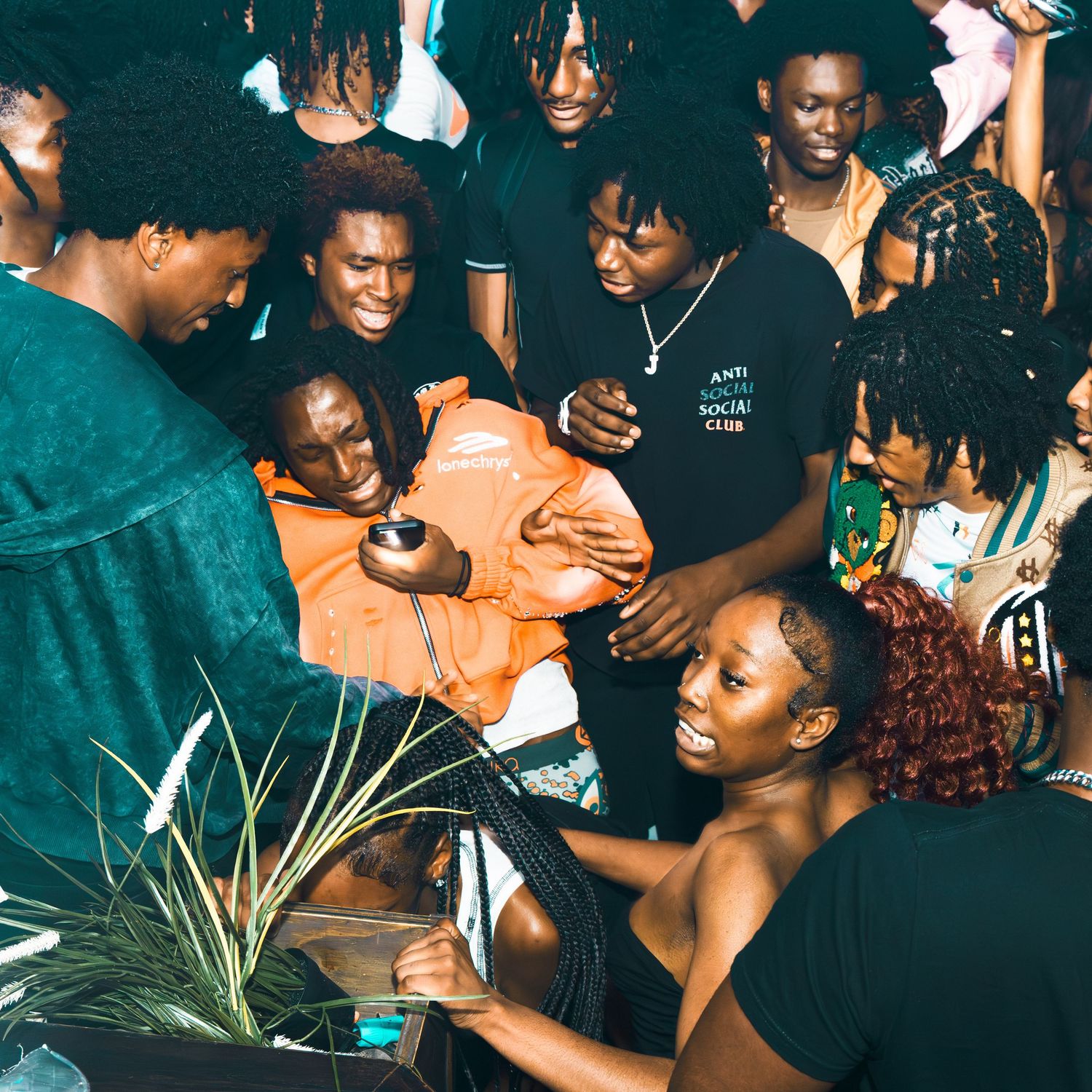 A lively group of young Black people gathered at a nightclub party, smiling and dancing together in a festive atmosphere.