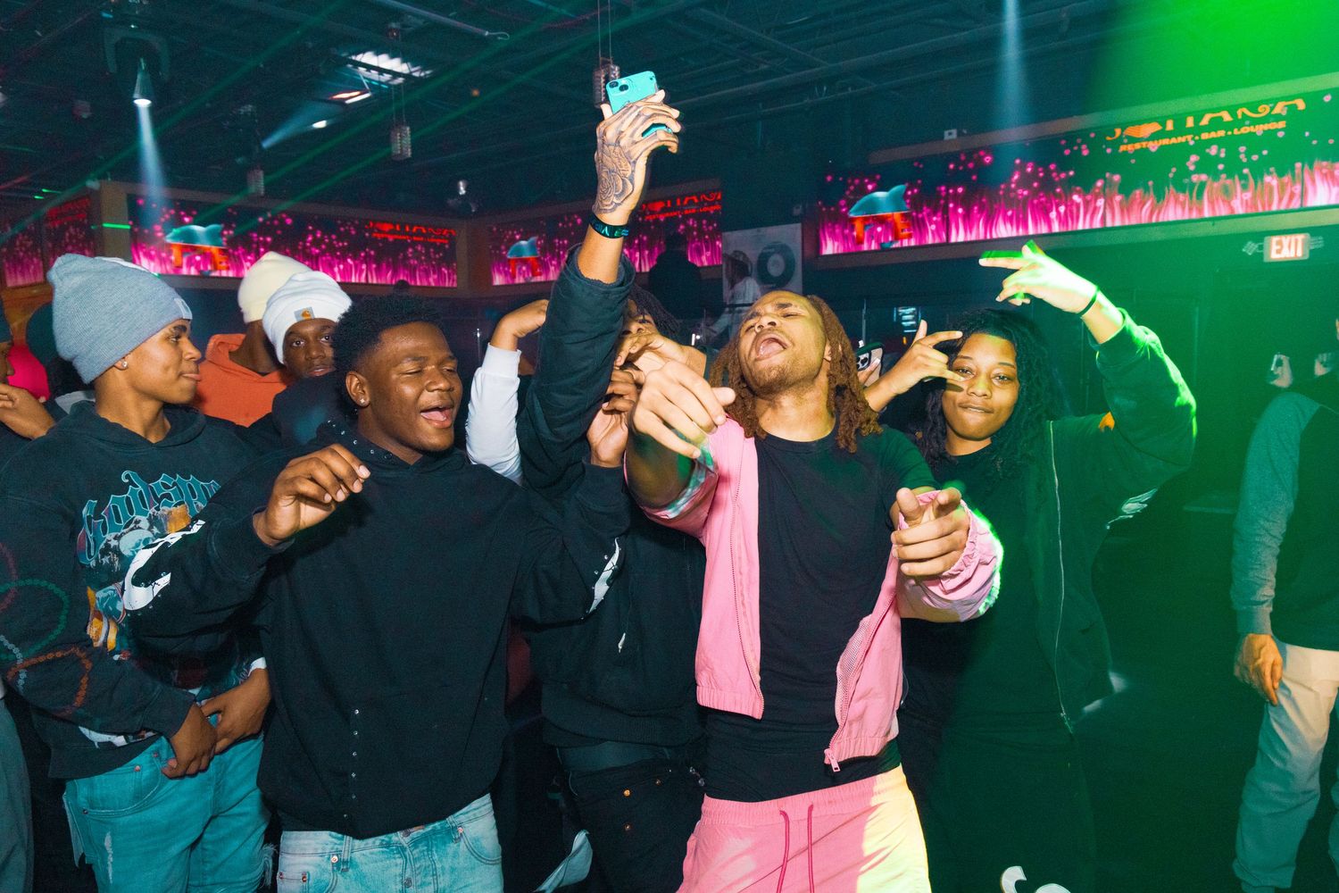 Group of young people dancing and celebrating at a vibrant nightclub with colorful neon lights.