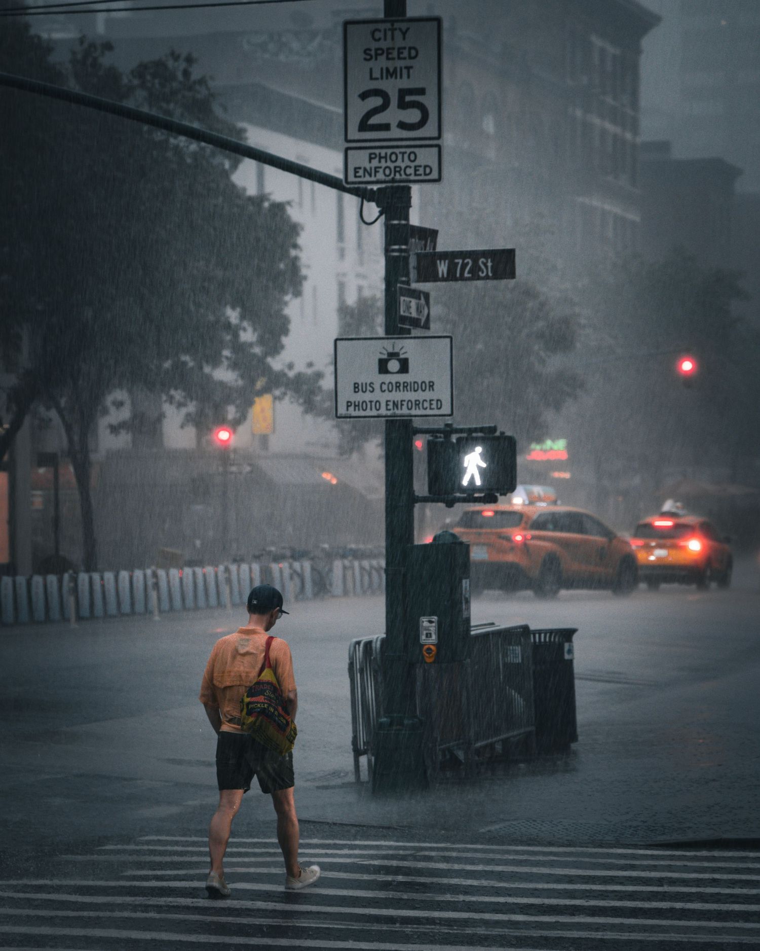 Person crossing rainy NYC street at W 72nd St intersection with speed limit sign and glowing pedestrian signal.