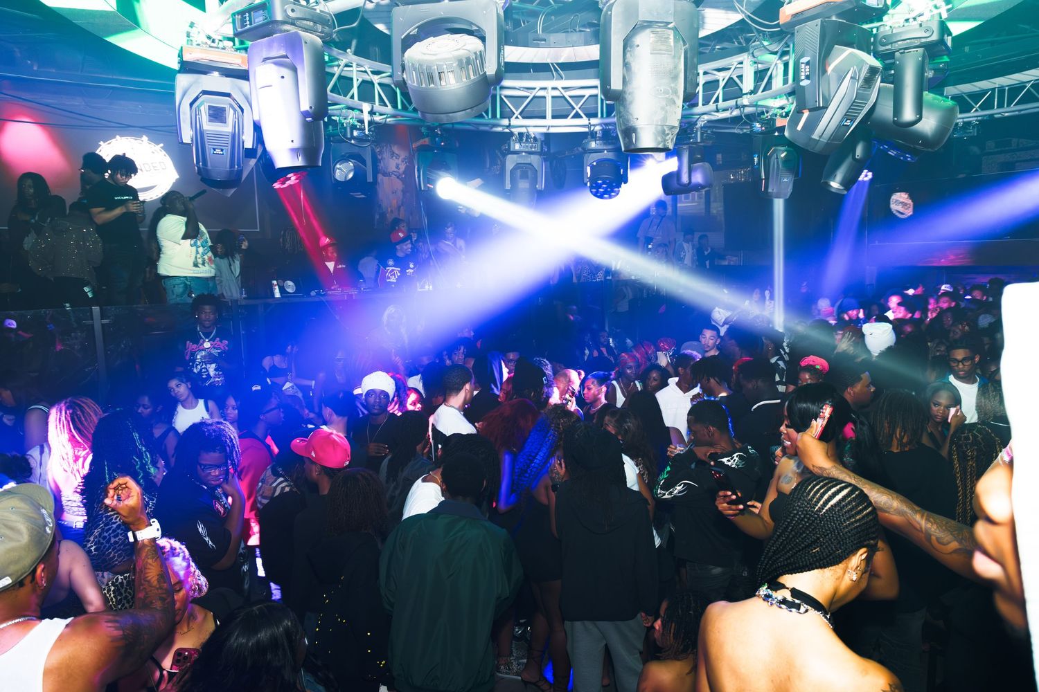 Crowded nightclub with blue and white laser lights illuminating a packed dance floor full of partygoers.