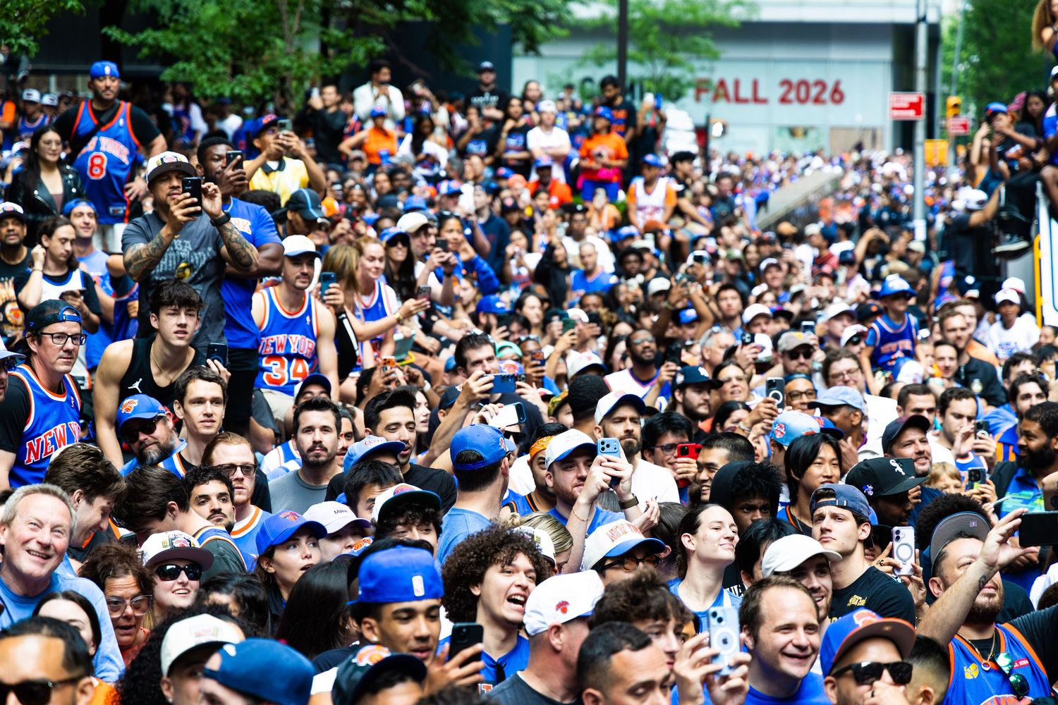 Large crowd of New York Knicks fans wearing blue and orange jerseys gathered outdoors at a rally event.