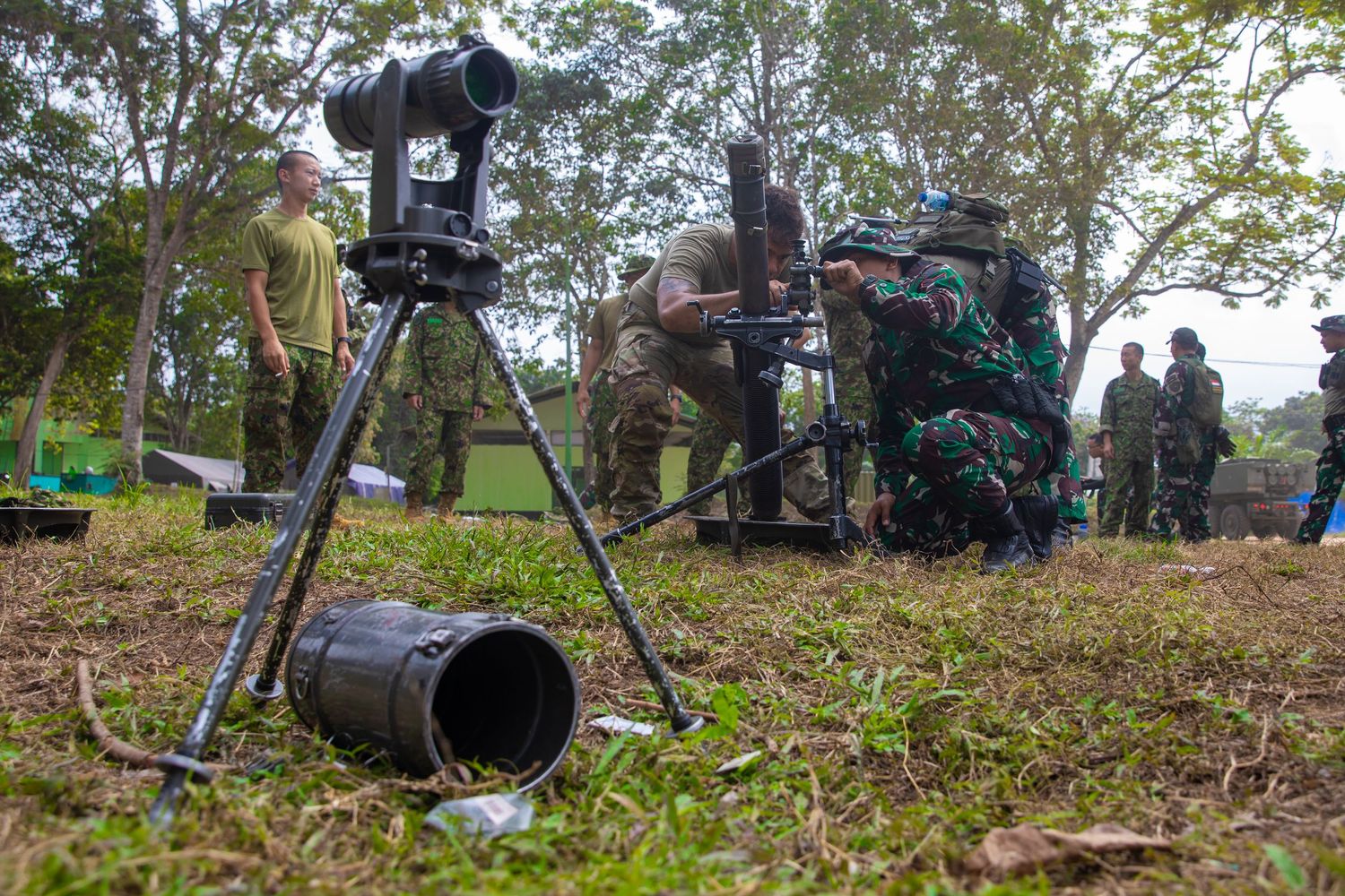 Military personnel operate surveillance equipment on a tripod during a multinational joint field training exercise.