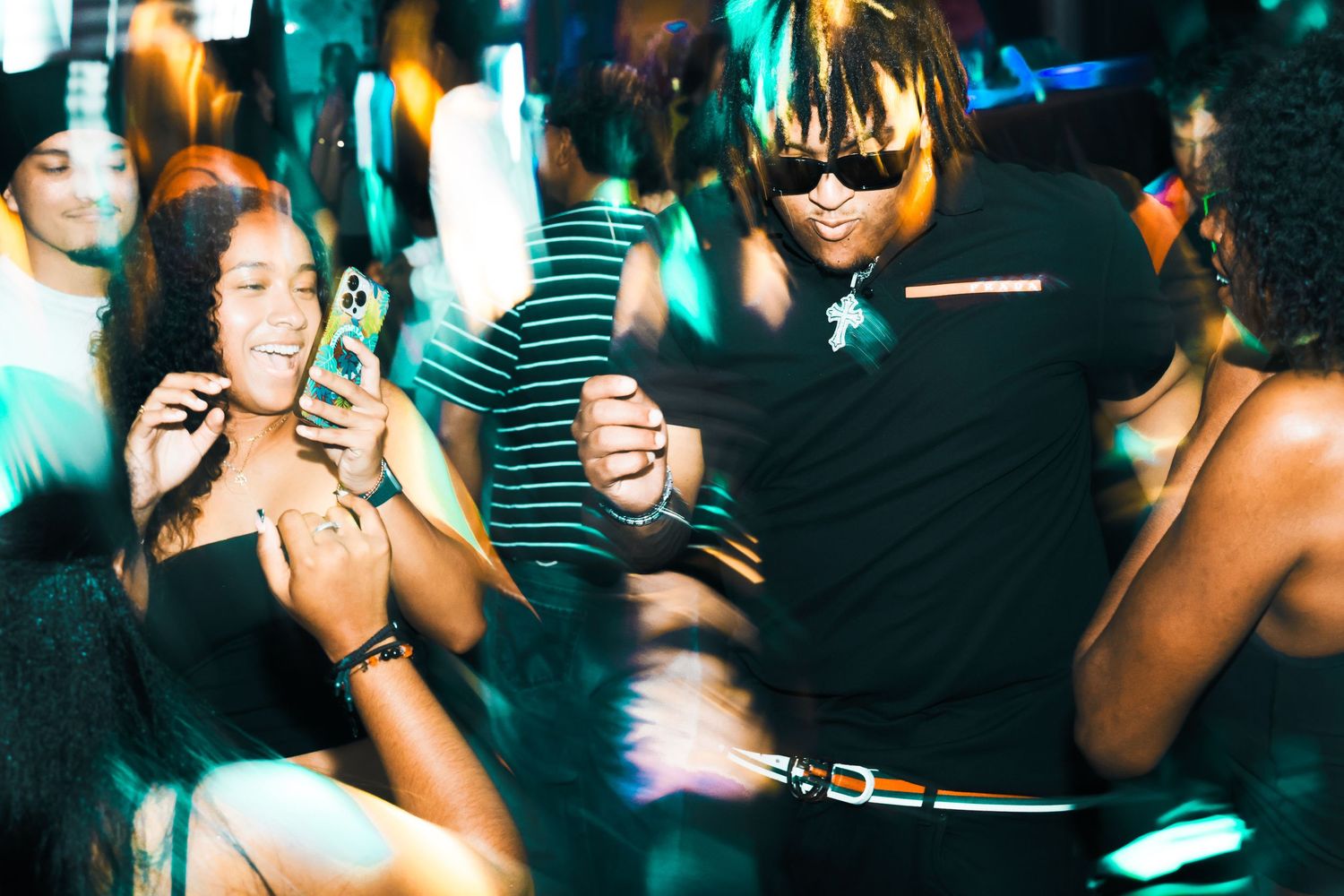 People dancing and taking photos at a vibrant nightclub party with colorful green lighting.