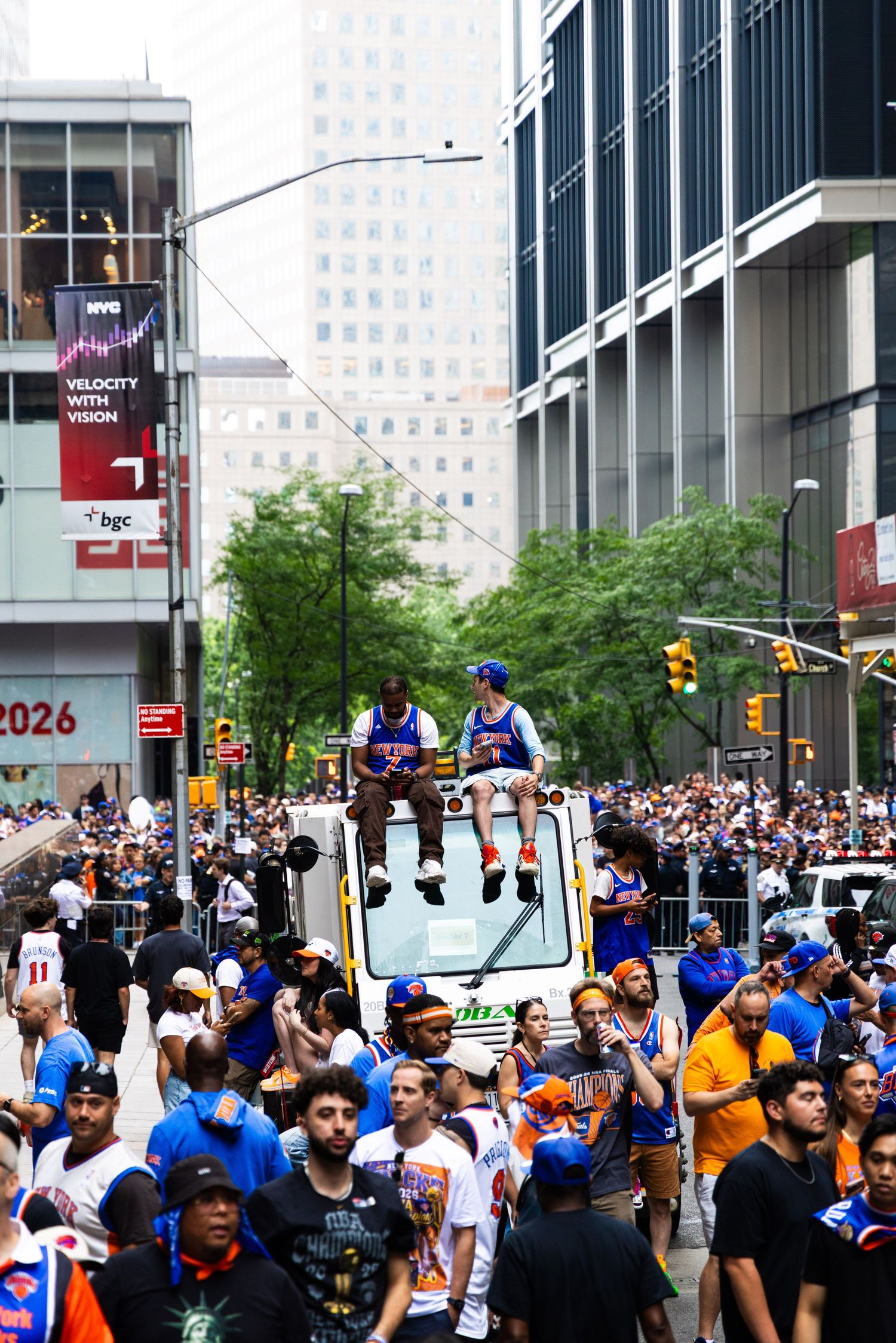 New York Knicks fans celebrate a parade on a crowded Manhattan street with players riding atop a vehicle.