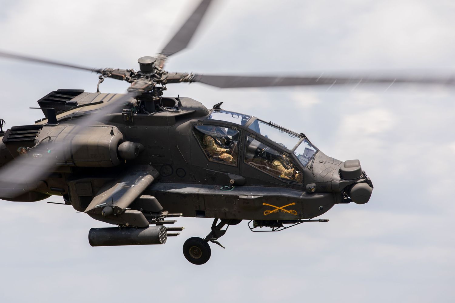 Close-up of AH-64 Apache attack helicopter in flight showing cockpit and weapons systems.