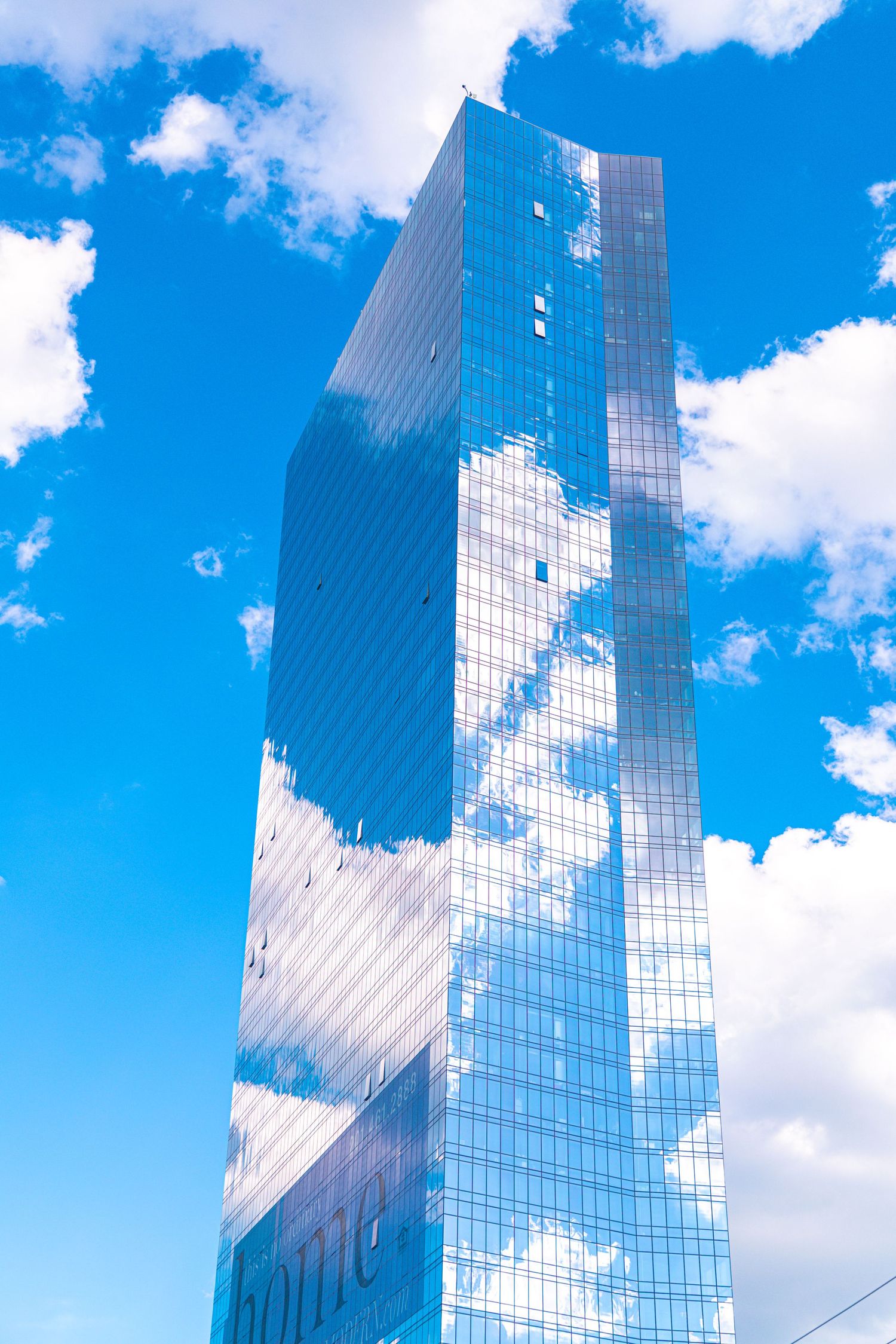 Glass skyscraper reflecting white clouds against a bright blue sky, showcasing modern architecture.