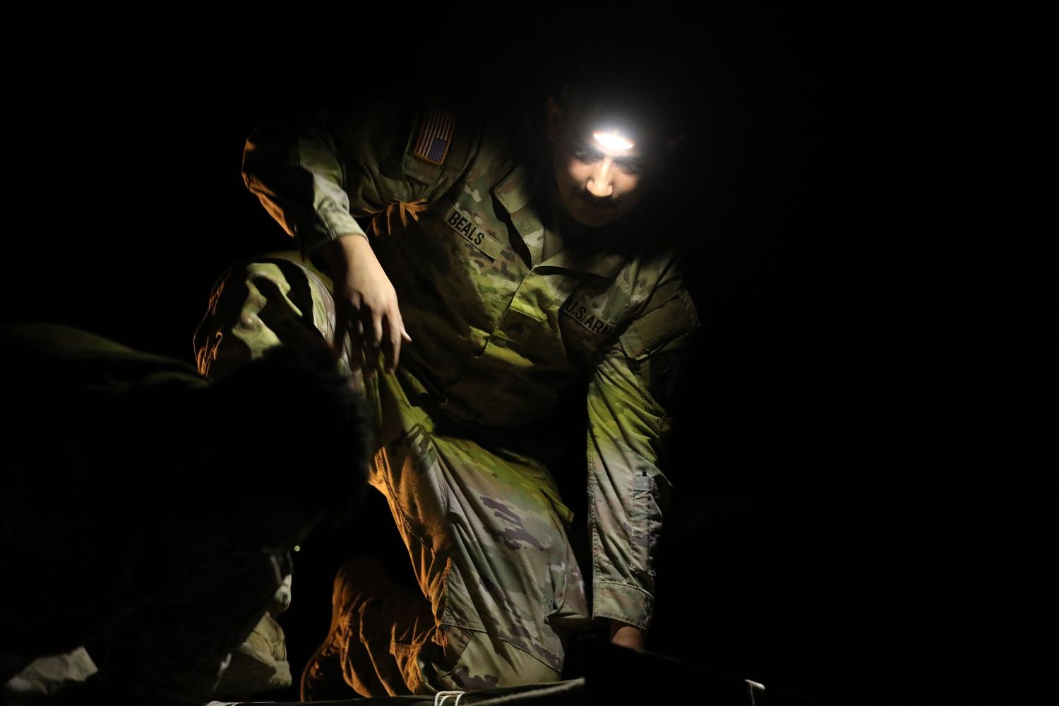 Soldier in camouflage uniform with headlamp working by firelight in complete darkness during a night military operation.