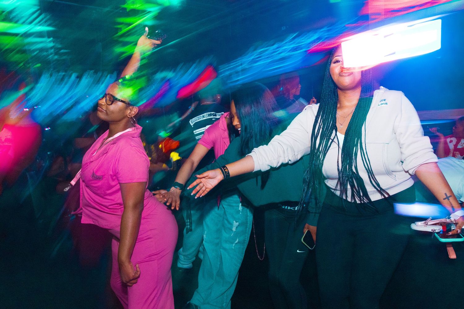 Two women dancing energetically at a vibrant nightclub with colorful neon lights in the background.