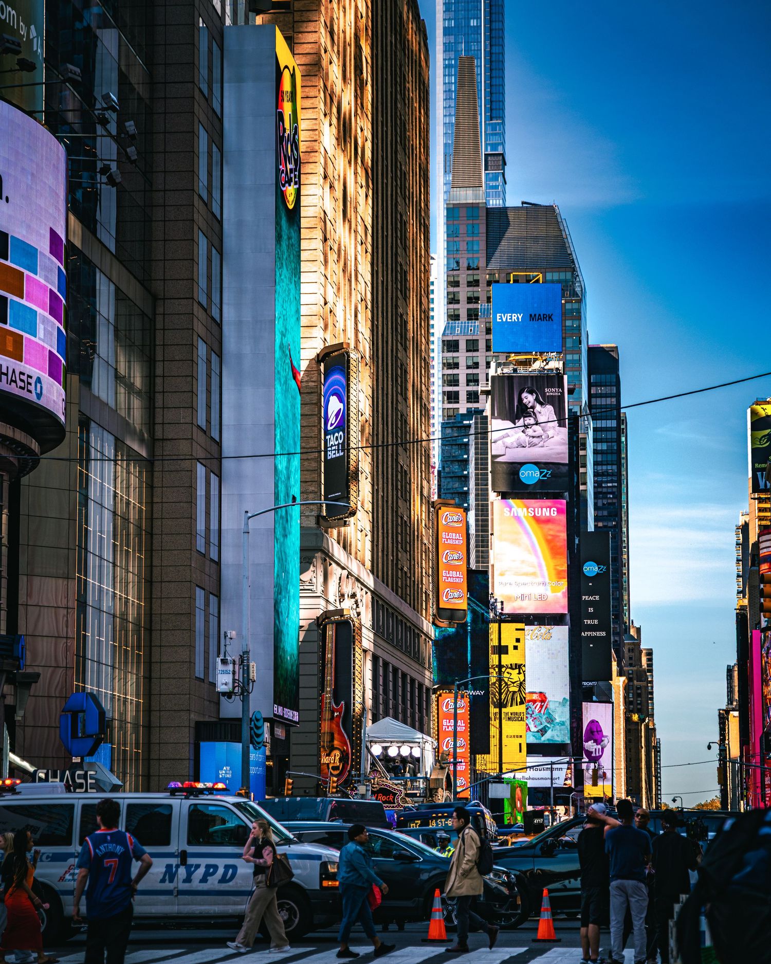 Busy Times Square NYC street scene with NYPD vehicle, colorful billboards, skyscrapers, and pedestrians under a blue sky.