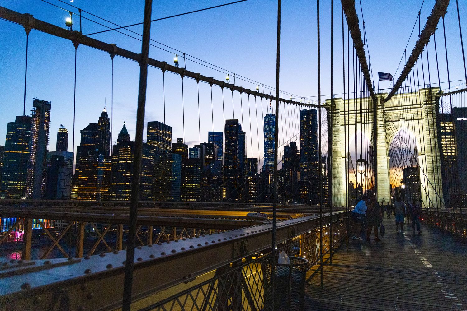 Brooklyn Bridge pedestrian walkway at dusk with illuminated Manhattan skyline in the background, New York City.