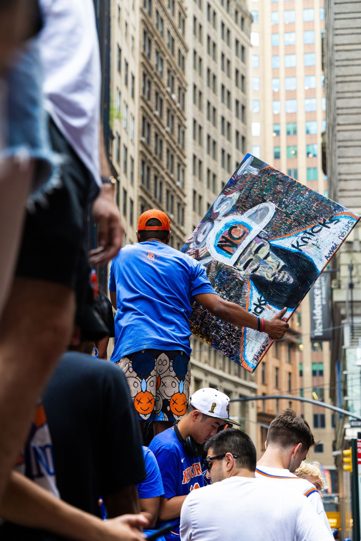 Fans hold a Knicks mosaic sign at a NYC street parade, surrounded by crowds in blue and orange team gear.