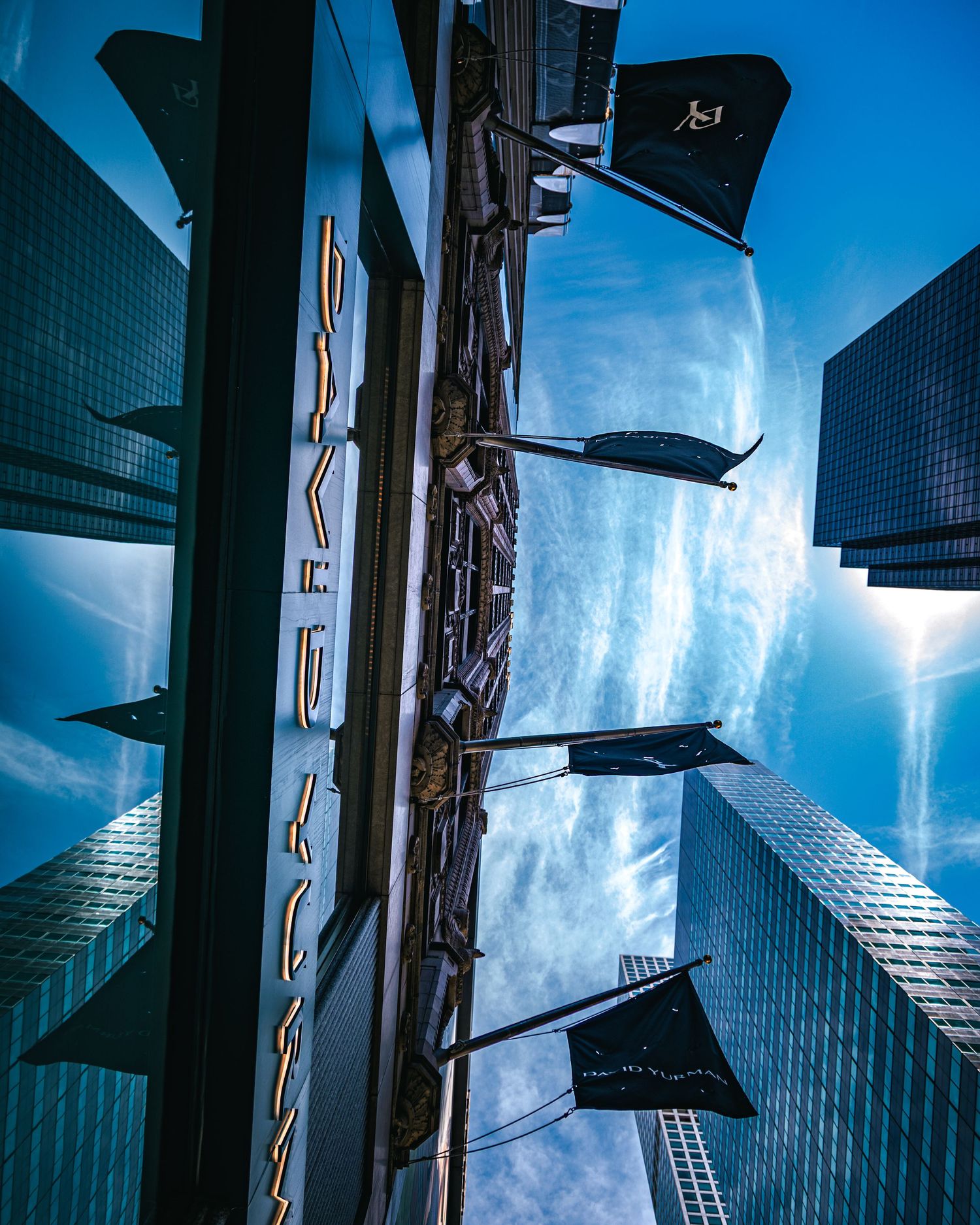 Dramatic low-angle view of skyscrapers and black flags against a vivid blue sky in an urban cityscape.