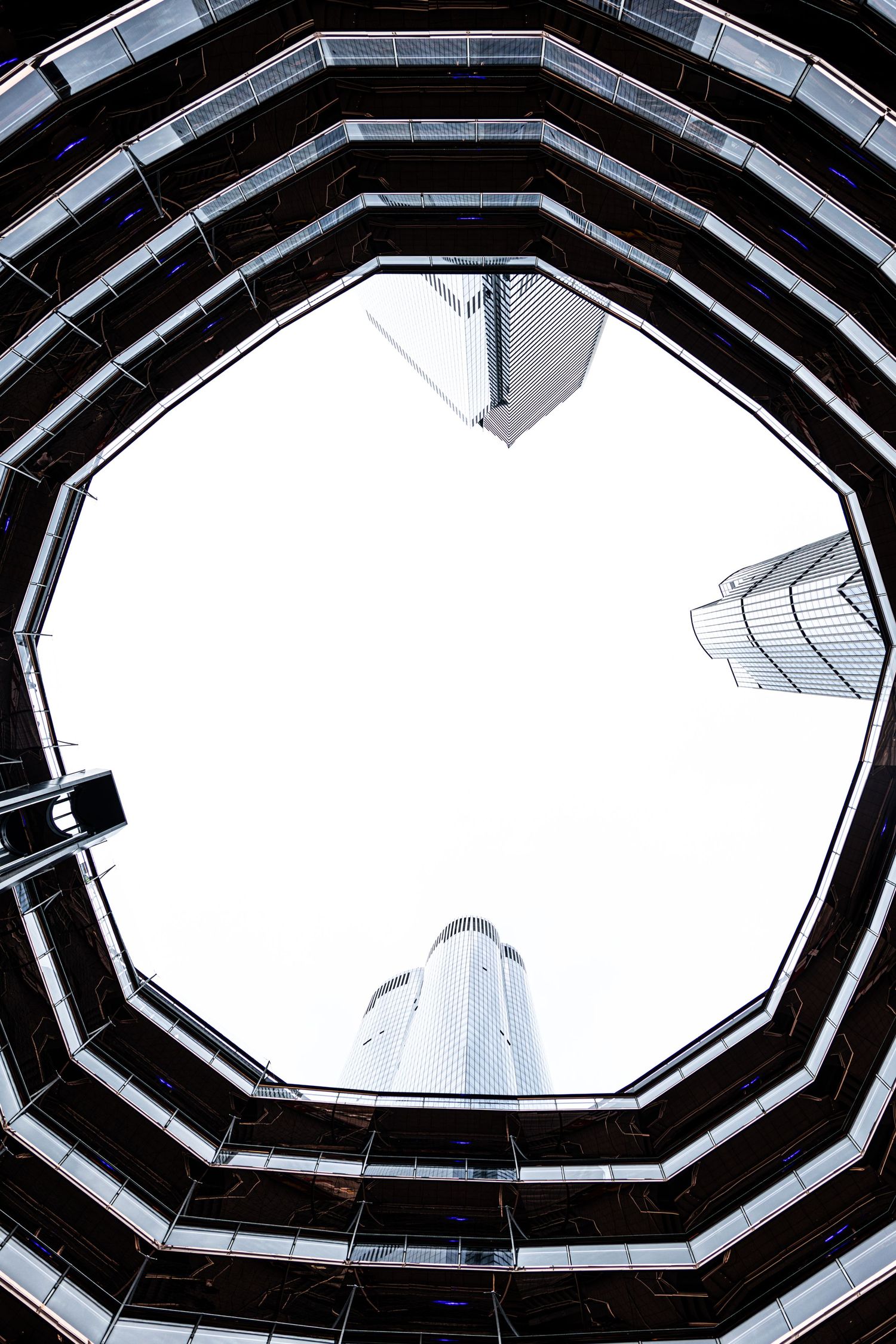 Looking up through an octagonal glass atrium at modern skyscrapers against a white sky.