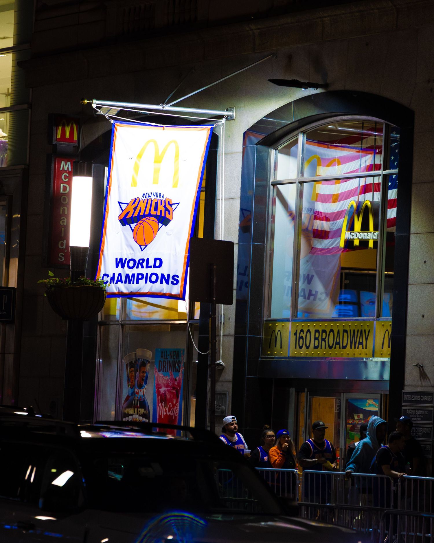 New York Knicks World Champions banner hanging outside 160 Broadway McDonald's at night in NYC.