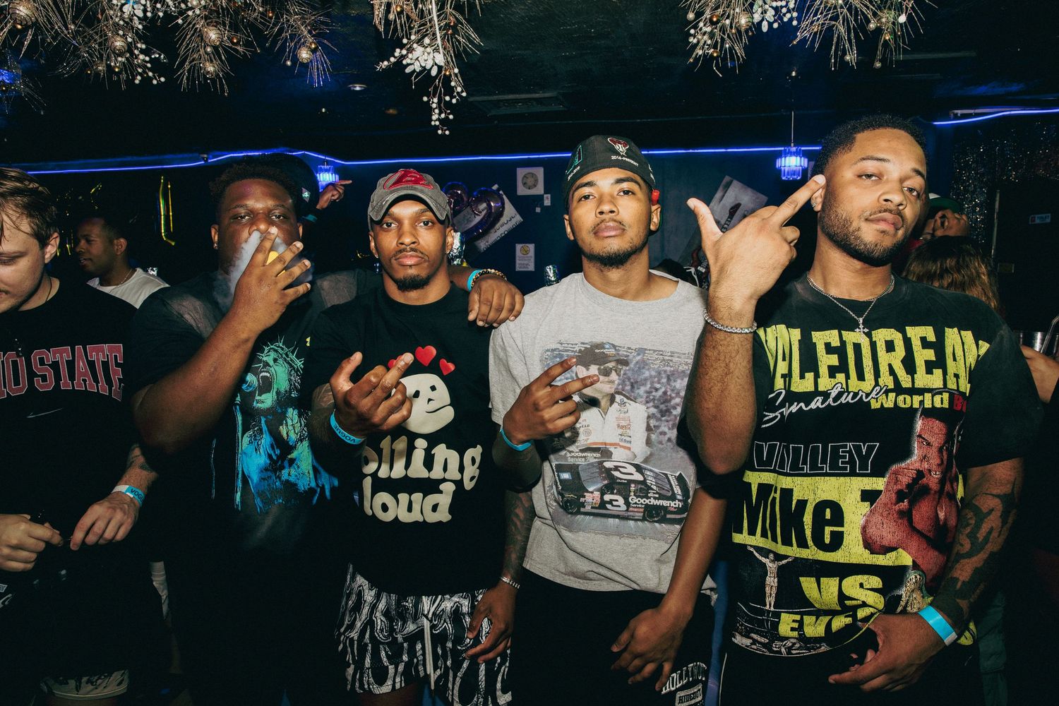 Group of men posing together wearing graphic tees at a nightclub event.