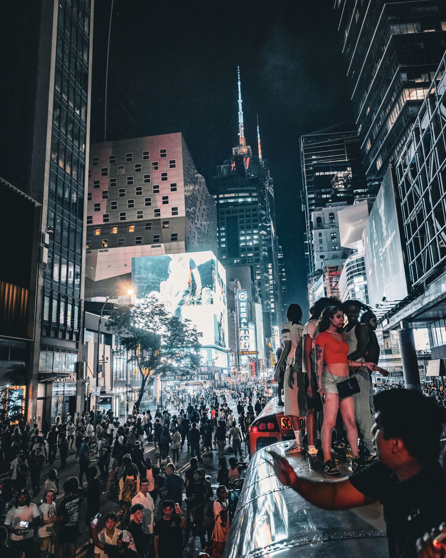 Crowded Times Square at night with illuminated skyscrapers and people standing on a vehicle in New York City.