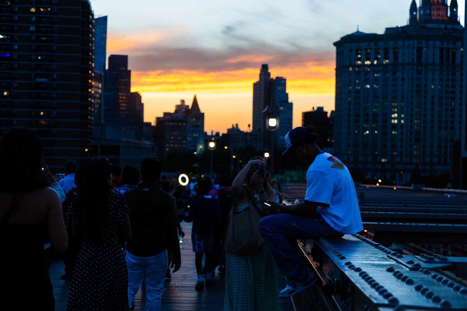 People gather on a rooftop overlooking a stunning orange and purple city sunset skyline at dusk.