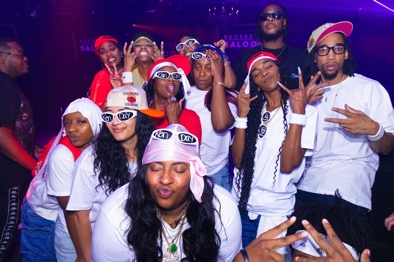 Group of friends posing together at a nightclub party, wearing white outfits and colorful accessories.