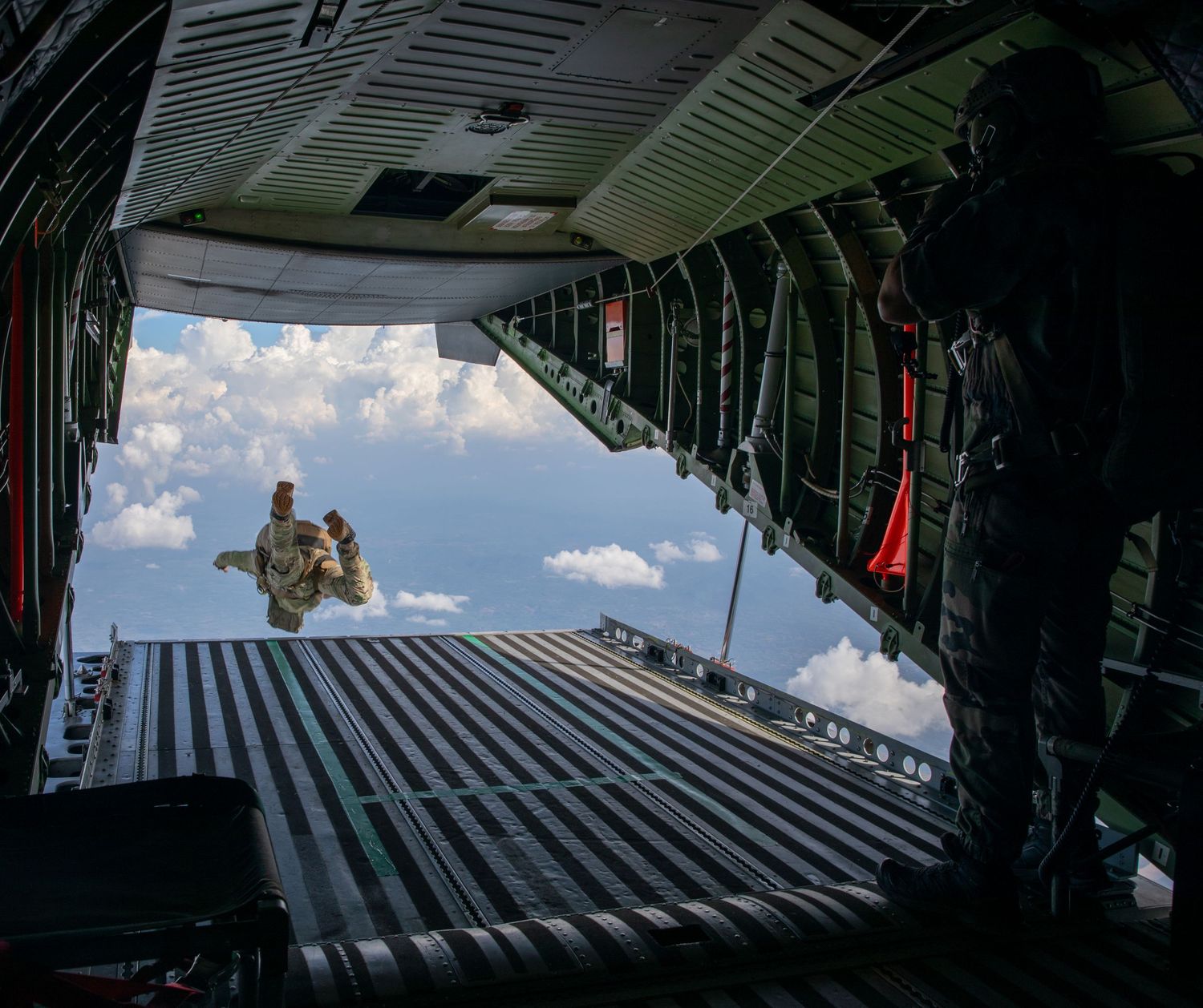 A soldier leaps from the open ramp of a military aircraft during an airborne parachute training exercise.